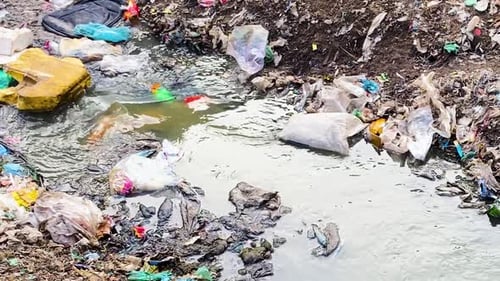 Stream Flowing among Heaps of Plastic Waste and Pollution
