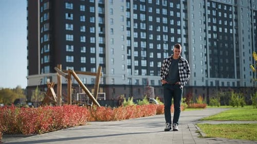 White Man Walking on Paved Path with Hands in Pockets Near Distant Pedestrian