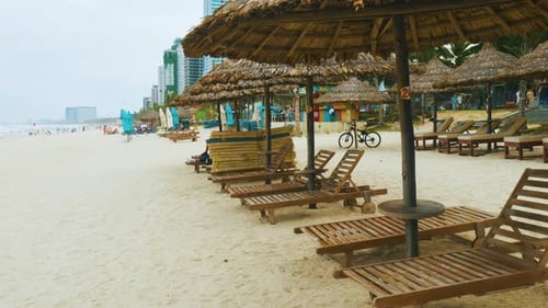 Wooden Sunbeds Lined Up Beneath Straw Umbrellas on Sandy Beach Tourists Wandering and Splashing in