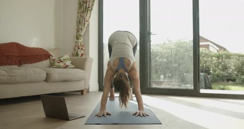 Mujer practicando ejercicios de yoga en casa viendo un vídeo tutorial en el ordenador portátil