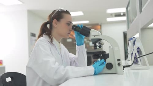 Woman in lab coat using microscope at lab