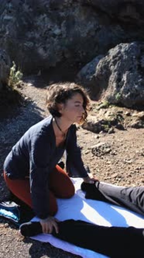 uma mulher faz uma massagem nos pés de um turista na natureza entre as pedras