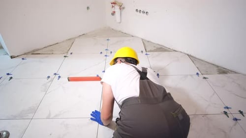 Construction Worker Tiling Bathroom Floor with White Marble Tiles