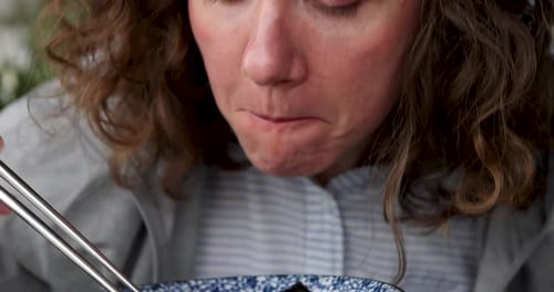 Gros plan d'une femme frisée mangeant de la soupe Pho Bo avec des baguettes en utilisant sa bouche, douce lumière naturelle