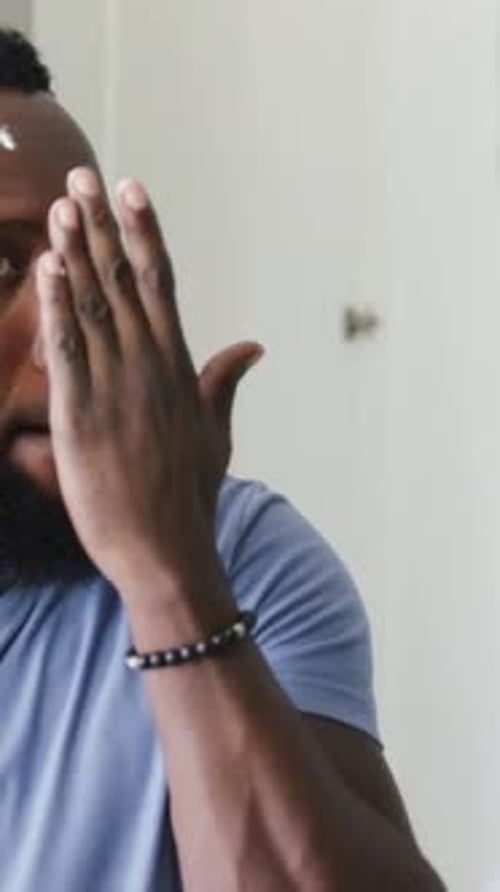 Vertical video: Noticing blemish in mirror man checking under eye in bathroom, showing bracelet