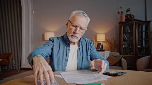 Senior Man Counting Money at Table Indoors