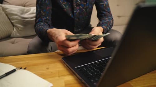 Man Counting Money with Laptop at Home