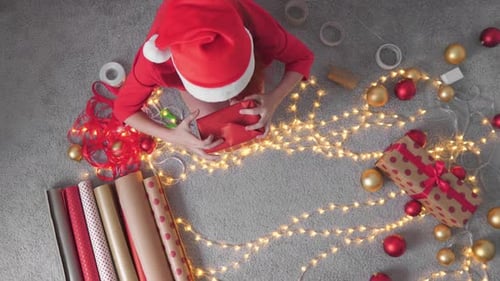 Woman Wrapping Christmas Gift on Floor with Lights