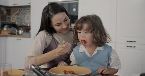 Woman Feeds Child at Kitchen Table
