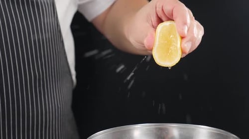Der Küchenchef presst Zitronensaft in Superzeitlupe auf schwarzem Hintergrund aus und presst Zitrone und Saft von Hand aus