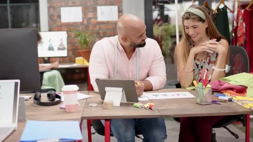 Happy diverse female and male designer discussing designs at fashion studio, in slow motion