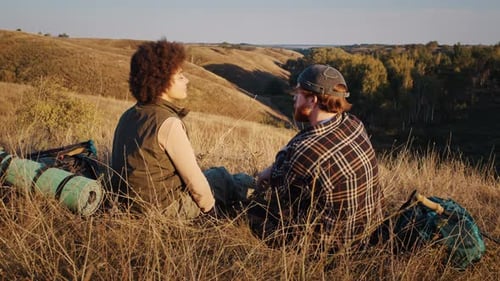 Happy Man and Woman Hikers Sit on Hill Top at Sunset Countryside