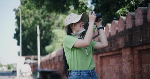 A young Asian woman stands on the side of the road and enjoys taking pictures with a camera.
