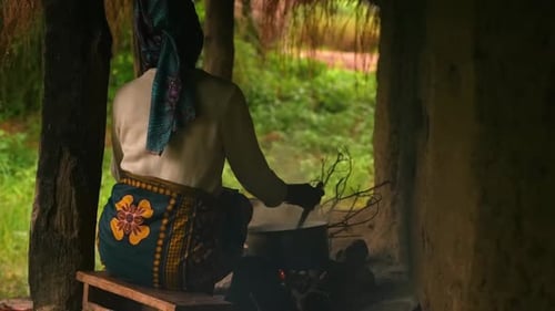 African woman cooking. Tending a pot over firewood