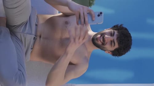 Man Lounging Shirtless Near Pool Uses Phone