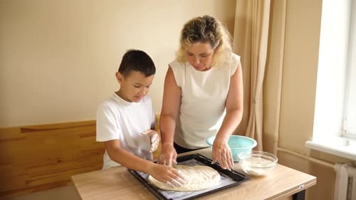 Boy and Woman Pressing Dough on a Tray