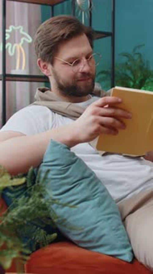 Man Reading Book Relaxing on Couch Indoors