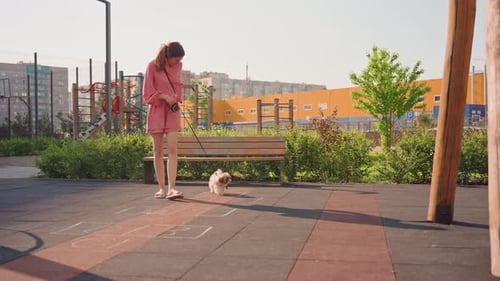 Person In Pink Attire Walks Small Dog Through City Park Casual City Resident Strolls With Pet Past