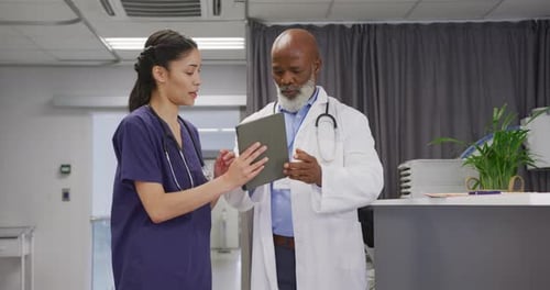 Diverse male and female doctors using tablet and talking at hospital