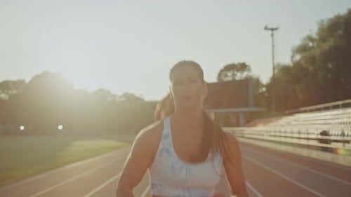 Beautiful Fitness Woman in Light Blue Athletic Top Jogging in an Outdoors Stadium. She is Running o