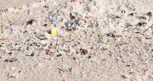 Close-up of microplastics pollution on sandy beach, environmental issue