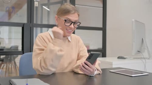 Female Worker Celebrating Success on Phone in Office