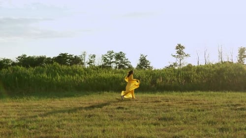 Drone Filming of Young Girl in Yellow Dress Running on Meadow Towards Road Slow Motion