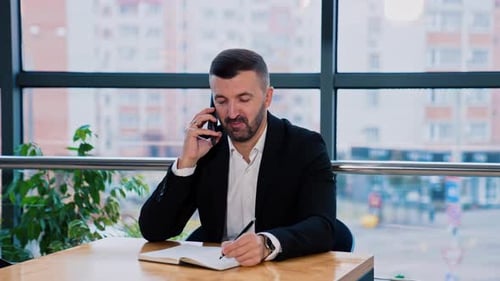 Man Talking on Phone and Writing at Table