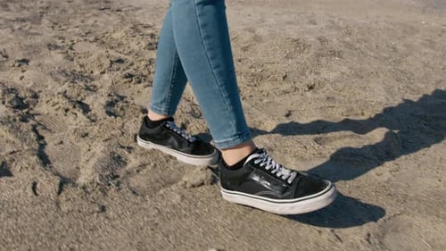 Walking on Sandy Beach in Jeans and Sneakers