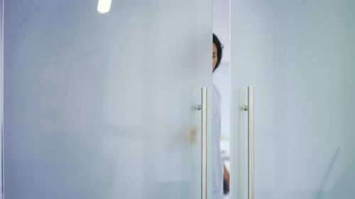 Young female employee in a blue shirt opens a glass door in a modern building and walks out