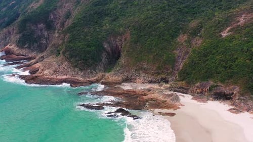 Peaceful sandy beach near rocky coastline of tropical island with green hills washed by turquoise se