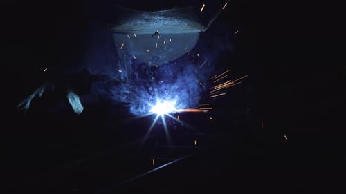 A blacksmith with a welding mask and welders leathers, is welding metal products in the garage, fire