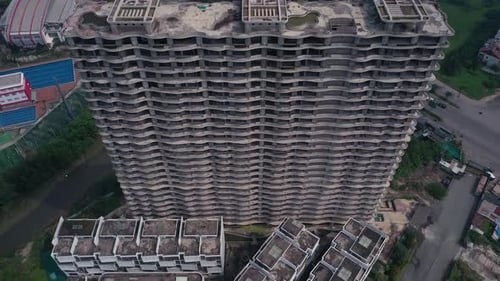 Aerial tilt down looking down facade of abandoned concrete shell of residential high-rise real estat