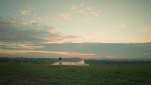Serene Sunset with Woman in White Dress By Lake in Tranquil Grassy Field