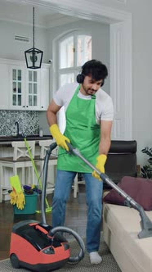 Man Wearing Apron Vacuums Couch in Living Room