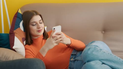 Concentrated Girl Typing on Smartphone at Home Young Woman Lying on Sofa