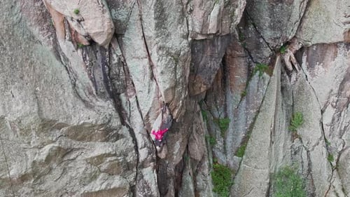 Bergsteiger erklimmt eine steile Felswand in einer pinken Jacke