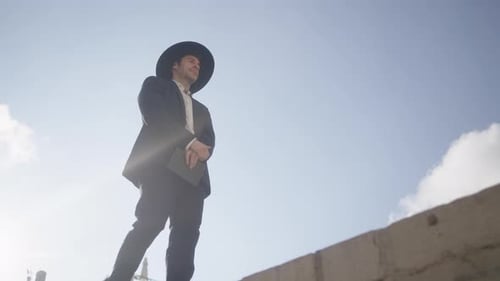 Low angle shot of an orthodox man in black suit and hat walking on a sunny day.