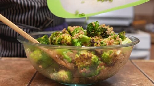Stirring green onions or scallions into a freshy fried and steaming broccoli dish with other ingredi