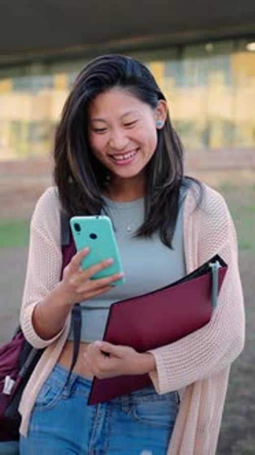 Niña de escuela china vertical sonriendo usando un teléfono celular para compartir fotos en la Aplicación de Redes Sociales en