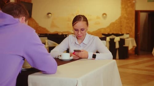 Young Man and Woman Browsing Mobile Phone Sitting in Restaurant