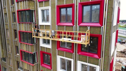 Aerial View Worker in a Cradle Install the Window Trim of a Multi-storey Building under Construction