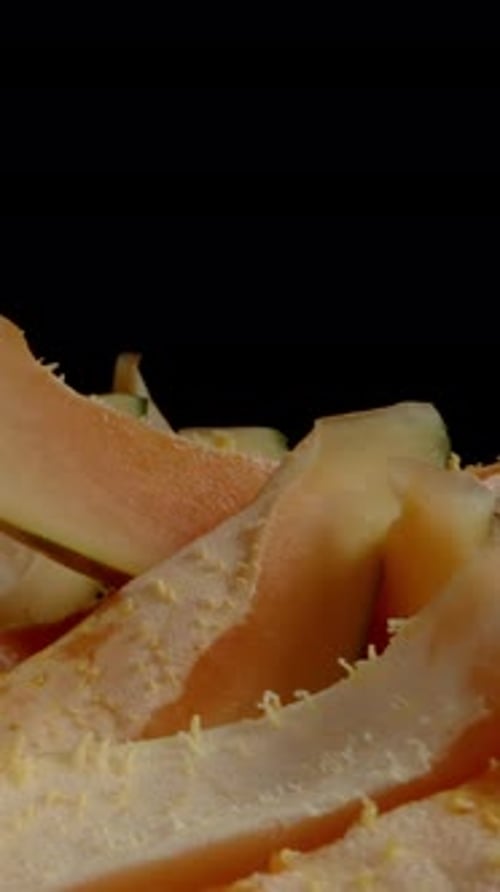 Vertical video. Sliced Seedless Papaya Wedges on a Black Background. Dolly slider extreme close-up.