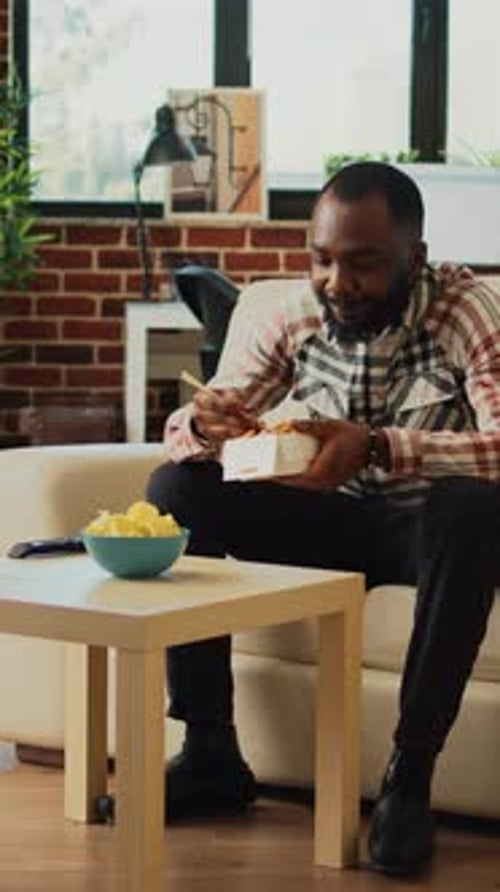 Man Eating Noodles Comfortably on Couch at Home