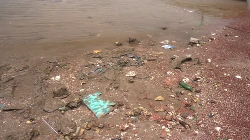 A littered beach with scattered debris and a distant rocky shoreline on a cloudy day