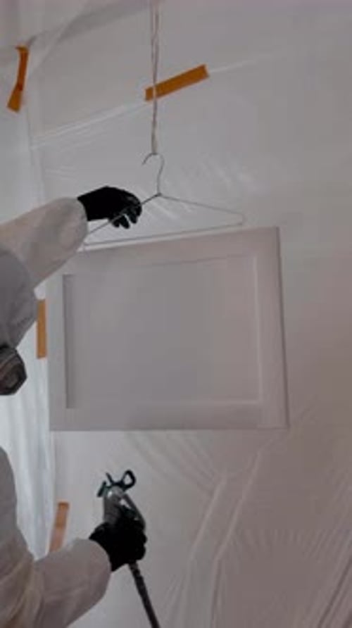 Fotografía vertical de un trabajador que usa una pistola rociadora para aplicar pintura o revestimiento dentro del gabinete durante la renovación