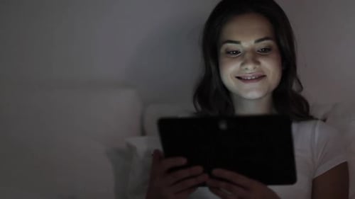Woman relaxes in bed using tablet at night