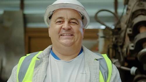 Portrait of an experienced senior male factory worker. He uses a tablet, then looks up and smiles