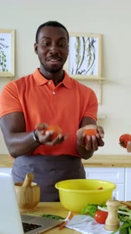 Homme en chemise orange jonglant habilement avec les tomates dans une cuisine lumineuse avec des ingrédients frais
