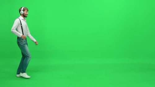 Passerby Cheerful Man in a White Shirt Walks on a Green Background Dancing and Listening to Music